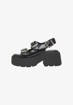 Black platform sandals with two metal buckle straps, a textured rubber sole, and a smooth leather upper, featuring a chunky silhouette.