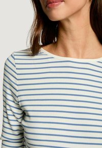 Maglia a manica lunga a coste di colore bianco con sottili righe orizzontali blu. Presenta un ampio scollo rotondo e una silhouette aderente.