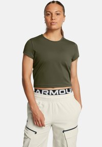 Camiseta corta de color verde oliva, hecha de una tela elástica y suave. Mangas cortas y escote redondo. Combinada con pantalones cargo de color claro.