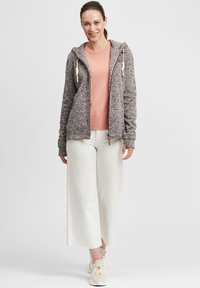 Grå stickad zip-up hoodie med dragsko, kombinerad med en rosa T-shirt och vita vida byxor. Skorna är beige med snörningsdesign och texturerade detaljer.
