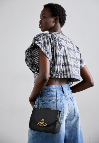 Geantă de piele neagră cu un emblema aurie, formă structurată și o curea subțire pentru umăr. Modelul poartă un top scurt cu carouri și pantaloni scurți din denim.