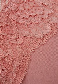 Roze kant stof met gegolfde randen, gelaagd over een zachte roze stof, met ingewikkelde patronen en een gestructureerd oppervlak.