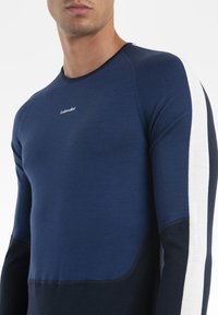 Man wearing a navy blue long-sleeve shirt with a white vertical stripe on the sleeve and small "icebreaker" logo on the chest.