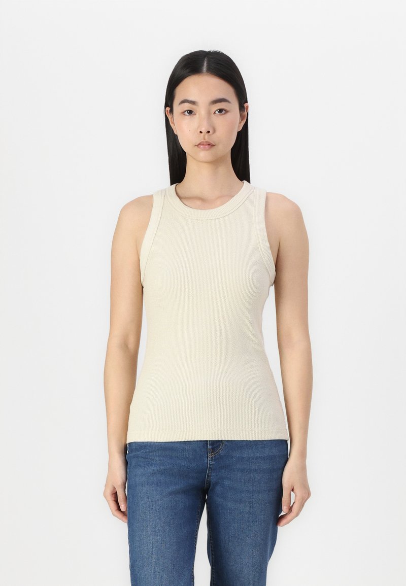 Beige ribbet t-skjorte med rund hals og brede stropper, tettsittende silhuett kombinert med blå jeans. Enkelt tekstur, ingen synlige mønstre.