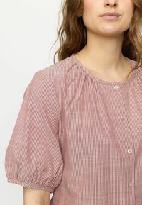 Röd och vit randig blus med korta puffärmar, rundad halsringning och knäppning framtill. Lättviktsmaterial med subtil textur.