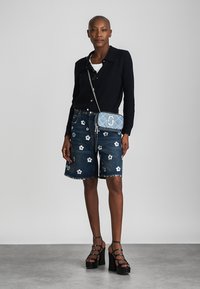 Tamsiai mėlynas juostuotas marškinėliai, džinsiniai šortai su baltais gėlės siuvinėjimais, juodis platforminiai sandalai su dirželiu ir mėlynas apgalvotas per petį krepšys.