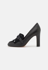 Scarpa nera in pelle con tacco alto, punta affilata, dettagli in suede e un fiocco decorativo. Presenta una superficie liscia e un tacco a spillo.