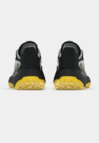 Μαύρα και γκρίζα αθλητικά παπούτσια με κίτρινα λαστιχένια πέλματα, με υφή και ενισχυμένο σχεδιασμό στη φτέρνα για σταθερότητα.