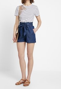 Chemise rayée à manches courtes avec un détail de feuille décoratif, associée à un short en denim taille haute et des sandales à brides marron.