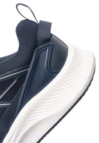 Detailní záběr paty atletické boty tmavě modré barvy s texturovanou pletenou tkaninou, poutkem a silnou bílou polstrovanou podrážkou s vzorovaným běhounem.