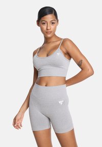 Sivina športna naprava, ki vključuje oprijet top s tankimi naramnicami in hlače z visokim pasom. Narejena je iz raztegljivega materiala, z diskretno logotipno podrobnostjo.