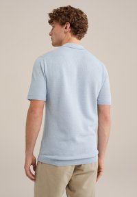 Tricou polo tricotat de culoare albastru deschis, cu mâneci scurte, guler și tiv cu dungi, afișând un material texturat pe un fundal neutru.