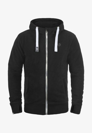 Svart fleece hettegenser med full glidelås, hvite snorer, sidelommer, ribbede mansjetter, og en subtil logo på brystet. Myk tekstur.