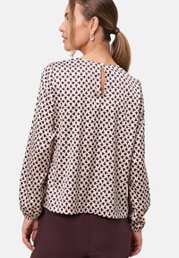 Langärmlige Bluse mit rundem Ausschnitt, die ein geometrisches Muster in Bordeaux und Creme auf leichtem Stoff zeigt, mit einem Rückenschlitz.