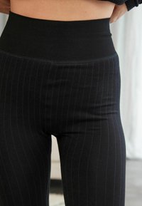 Sorte ribbede leggings med høj talje, prydet med subtile lodrette striber, glat tekstur og tætsiddende design.