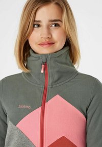 Giacca in pile grigia con colletto alto, presenta motivi geometrici rosa e rossi e una zip a contrasto in rosa e nero. Logo del brand sul petto.