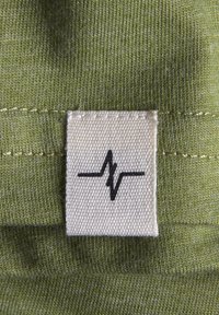 Groene stof met een gestructureerde afwerking, met een crèmekleurig label waarop een grafiek van een zwarte hartslaglijn staat. Gestikte randen zijn zichtbaar.