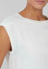 Weißes Kurzarmoberteil mit rundem Ausschnitt. Glattes, weiches Material mit leicht dehnbarem Textil. Minimalistisches Design, keine sichtbaren Muster oder Akzente.