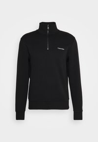 Pull noir à manches longues avec col demi-fermeture éclair et petit logo blanc Calvin Klein sur le côté gauche de la poitrine.