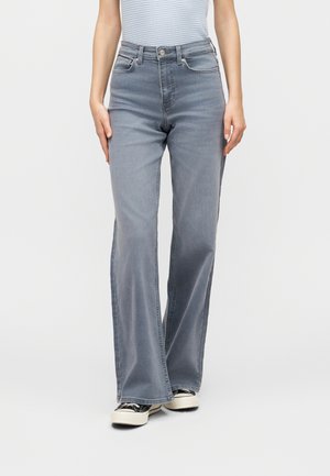 Femme portant un jean droit taille haute gris clair avec cinq poches et fermeture par bouton, associé à des baskets noires et blanches.