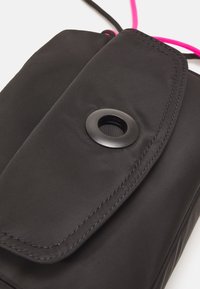 Sacchetto in tessuto nero con chiusura a patta, caratterizzato da un dettaglio a grommet nero circolare e accenti in corda rosa brillante. Superficie liscia, design minimalista.