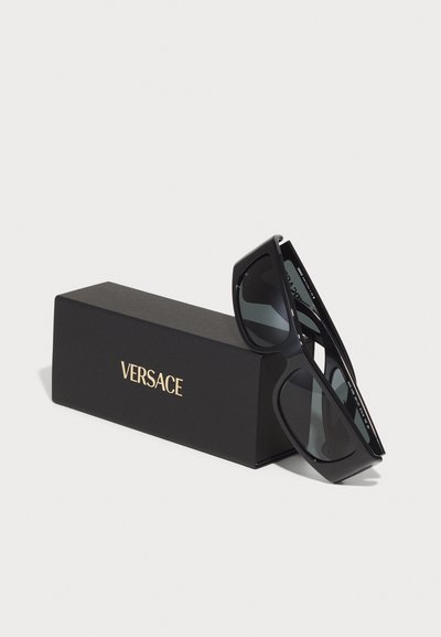 Juodos Versace saulės akinius su elegantišku, kampuotu dizainu, turinčiu tamsius objektyvus ir subtilų logotipą ant šventyklos, supakuotus juodame dėkle.
