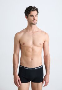 Schwarze Boxershorts mit einem breiten Bund, der das Logo "BJÖRN BORG" trägt. Glattes Material, figurbetontes Design und mittelhoher Schnitt. Das Modell steht vor einem neutralen Hintergrund.