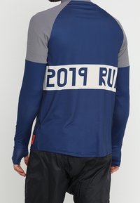Man wearing a long-sleeve blue and gray sports shirt with "2019 RU" text on the back, paired with black pants.