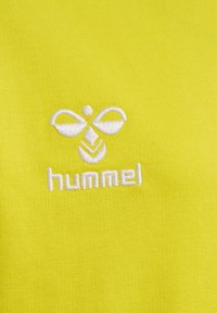 Tessuto giallo con una texture liscia che presenta ricami bianchi di un logo e la parola "hummel" in fondo.