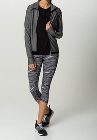 Šedá zipová bunda, černé tričko, vzorované černobílé capri legíny a černé sportovní boty s bílými akcenty.