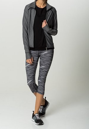 Šedá zipová bunda, černé tričko, vzorované černobílé capri legíny a černé sportovní boty s bílými akcenty.