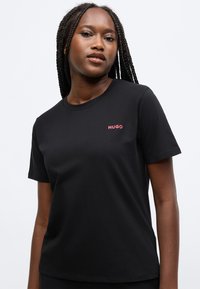 Fekete pamut rövid ujjú póló, kerek nyakkivágással és egy kis piros "HUGO" logóval a bal mellrészen. Simább textúra, klasszikus szabás.