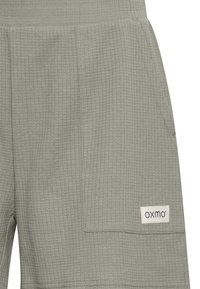 Gröna shorts med våfflat mönster, platt midjeband, sidficka och en broderad logotags. Designen är enkel och funktionell.