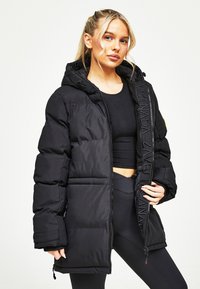 Melna pūkņu jaka ar kapuci, kas aprīkota ar rāvējslēdzēju priekšpusē un logo detalizāciju gar rāvējslēdzēju. Tekstūras materiāls ar polsterējuma dizainu.