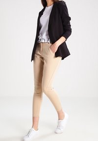 Beiga skräddarsydda byxor med slim fit, med sidsömmar och en mjuk textur. Matchas med en svart kavaj och vita sneakers.