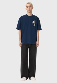 Granatowy, oversize'owy t-shirt z grafiką czaszki na piersi, zestawiony z luźnymi czarnymi dżinsami i białymi trampkami.