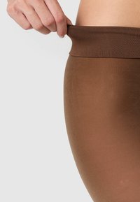 Leggings marroni con una texture liscia, dotati di un ampio elastico che viene tirato leggermente. Il materiale sembra elastico e aderente.
