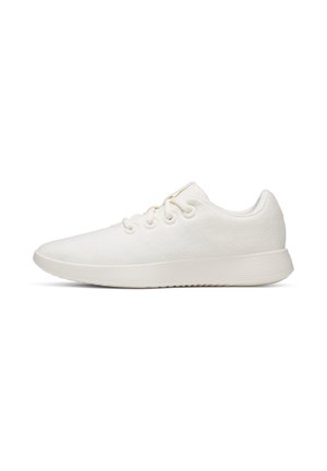 Weißer Sneaker mit niedrigem Schaft, Schnürsenkeln und einer geriffelten Sohle, seitlich auf weißem Hintergrund dargestellt.