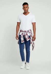 Άσπρη μπλούζα v-neck, μπλε στενές τζιν παντελόνες και άσπρα αθλητικά παπούτσια. Ένα κόκκινο και μπλε καρό πουκάμισο δεμένο στη μέση προσθέτει λεπτομέρεια στην εμφάνιση.