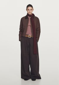 Brązowa kurtka z kołnierzem, różowy golf, brązowe spodnie z szerokimi nogawkami oraz burgundowy dzianinowy szalik. Posiada pasek ze srebrną klamrą. Czarne buty.