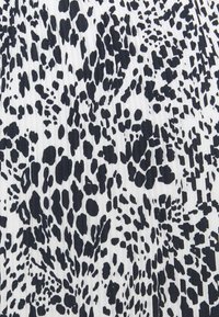 Hvidt stof med tæt pakket uregelmæssige sorte pletter, der skaber et abstrakt, dyreinspireret mønster og en let plisseret tekstur.