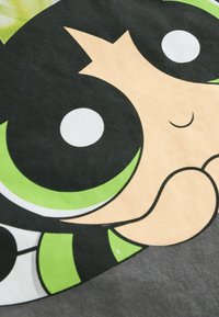 Grafisk t-shirt med et stiliseret karakteransigt med store sort-hvide øjne, grønne accenter og en blød, tekstureret stofbaggrund.