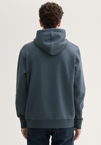 Tumed sinise kapuutsiga dressipluus, mis on valmistatud pehmest kangast. Omab känguru taskut ja soonikuid, ning lõige on taga vabalt langev.