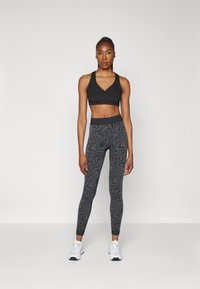 Black sports bra with a V-neck design paired with high-waisted leggings featuring a dark gray abstract pattern. White athletic shoes.
