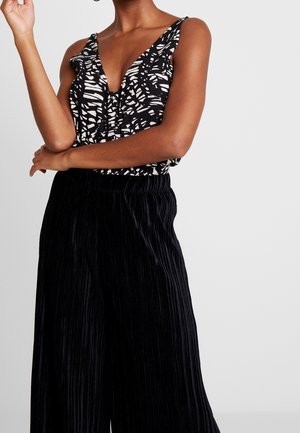 Zwart-wit top met patroon, diepe V-hals en ruches op de schouderbanden, gecombineerd met zwarte geplooide wijd uitlopende broek met elastische tailleband.