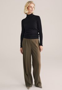 Juodas golfas, derinamas su aukštu liemeniu ir plačiomis žaliomis kelnėmis. Audinys su tekstūra, turintis lygų paviršių. Smailūs pilki batai.