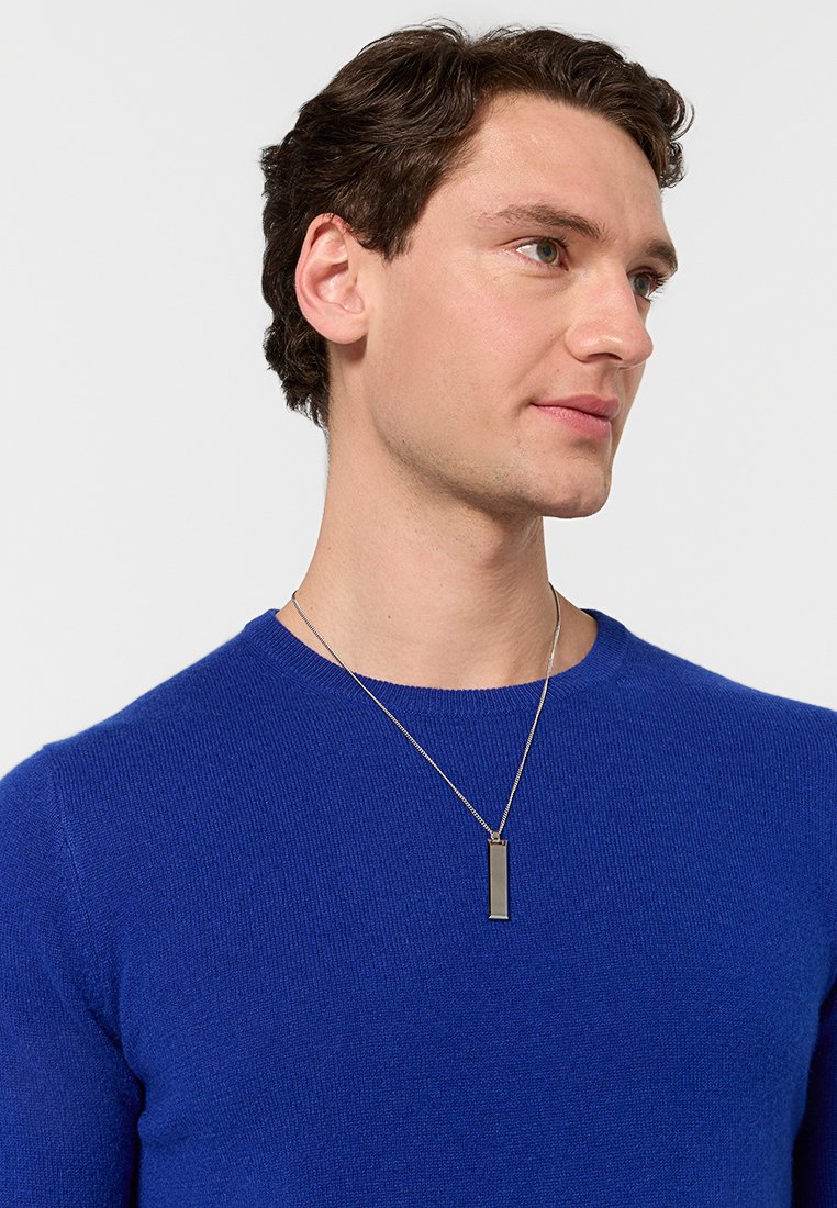 Silberne Kettenhalskette mit rechteckigem Anhänger, getragen mit einem blauen Pullover. Der Anhänger ist elegant und minimalistisch und hebt modernes Design hervor.
