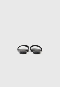 Svarta platta sandaler med två böjda remmar, minimalistisk design och sl�ät yta, med en låg sula för komfort.