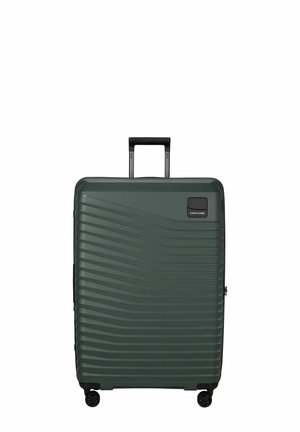 Valise rigide vert foncé avec une texture à vagues horizontales, quatre roues et une poignée noire rétractable déployée en position verticale.