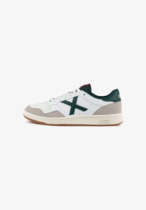 Zapatilla blanca con detalles en verde, materiales de malla y ante, puntera redonda, suela plana y distintivo logotipo "Munich" en el talón.